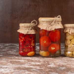 Pickled red peppers and mushrooms in a glass jar on marble table with bowl of pickled tomatoes. High quality photo
